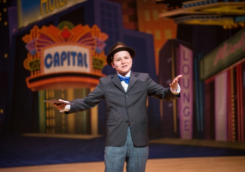 An FPAS student in a bow tie performing a solo in front of a painted Capital Theatre marquee