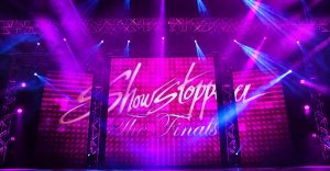 ShowStoppers stage graphic, white script lettering in magenta stage haze